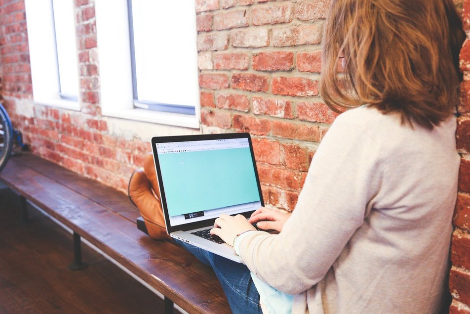 Eine Frau sitzt am Fenster und sucht einen freien Studienplatz am Laptop