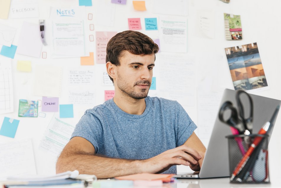 Studierender-am-Laptop-mit-Notizen-an-Wand